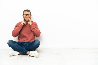 Genç yakışıklı bir adam yerde oturmuş mutlu ve hoş bir ifadeyle gülümsüyor.