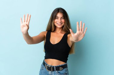 Mavi arka planda izole edilmiş genç beyaz kadın parmaklarıyla dokuzu sayıyor.