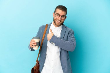 Kafkasyalı genç işadamı mavi arka planda izole edilmiş bir şekilde baş parmak hareketi yapıyor.