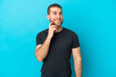 Genç yakışıklı beyaz adam mavi arka planda izole edilmiş yukarı bakarken bir fikir düşünüyor.