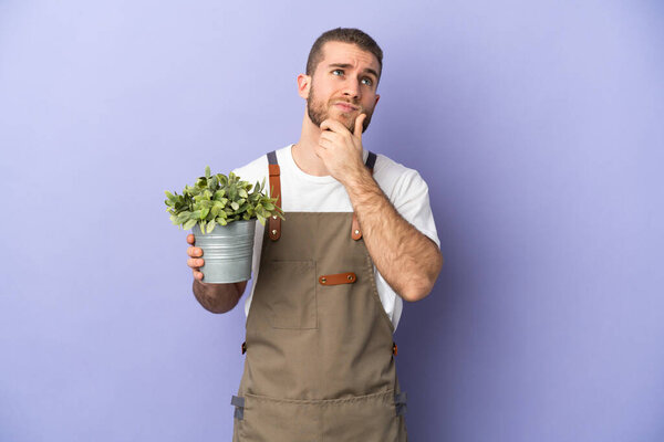 Gardener caucasian man holding a plant isolated on yellow background having doubts