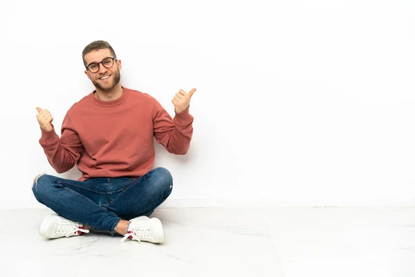 Mladý Pohledný Muž Sedící Podlaze Palci Nahoru Gestem Úsměvem — Stock fotografie