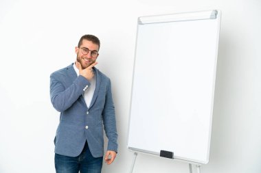 Beyaz arka planda izole edilmiş beyaz panoda sunum yapan genç iş kadını mutlu ve gülümsüyor.