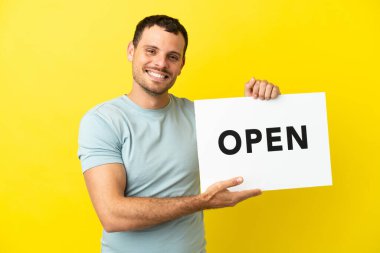 Mor arka planda yaşayan Brezilyalı bir adam elinde mutlu bir ifadeyle barış sembolü taşıyan bir levha tutuyor.