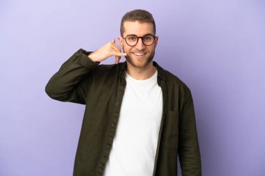 Mor arka planda izole edilmiş yakışıklı beyaz bir adam telefon jesti yapıyor. Bana geri dönüş işareti ver.