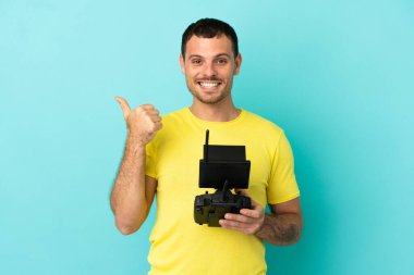 İzole edilmiş mavi arkaplan üzerinde uzaktan kumanda tutan Brezilyalı bir adam bir ürünü sunmak için yan tarafı işaret ediyor