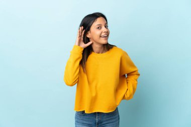 Kafkasyalı kız mavi arka planda izole edilmiş bir şekilde elini kulağına koyarak bir şeyler dinliyor.