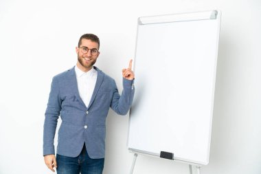 Beyaz arka planda izole edilmiş beyaz panoda sunum yapan genç bir iş kadını en iyinin işareti olarak parmağını kaldırıyor.