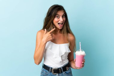 Çilekli milkshake 'i olan genç bir kadın mavi arka planda izole edilmiş bir şekilde baş parmak hareketi yapıyor.