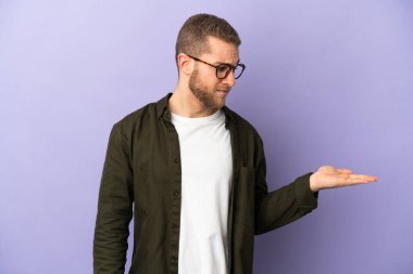 Mor arka planda izole edilmiş yakışıklı beyaz adam kopyalama alanını şüphe ile tutuyor.