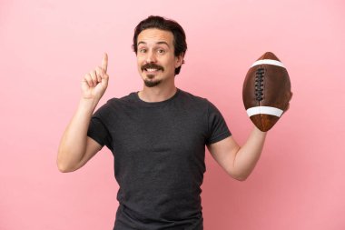 Genç beyaz adam rugby oynuyor. Pembe arka planda izole edilmiş. En iyinin işareti olarak parmağını kaldırıyor.