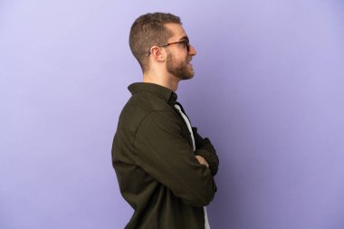 Mor arka planda yalıtılmış yakışıklı beyaz adam yan pozisyonda.