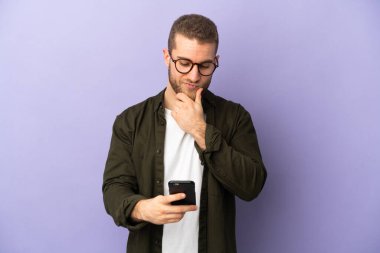 Mor arka planda izole edilmiş yakışıklı beyaz adam düşünüyor ve bir mesaj gönderiyor.