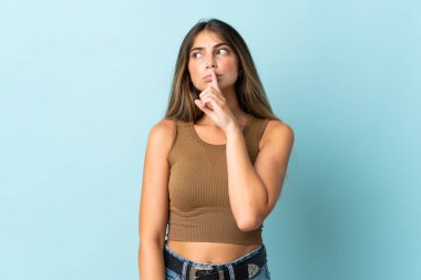 Mavi arka planda izole edilmiş beyaz bir kadın sessiz bir jest işareti gösteriyor. Parmağını ağzına sokuyor.