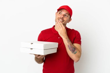 Pizza teslimatçısı üniformalı adam izole edilmiş beyaz duvardan pizza kutuları alıyor gülümserken yukarı bakıyor.