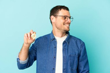 Tarafsız mavi arka plan üzerinde Bitcoin tutan Brezilyalı bir adam