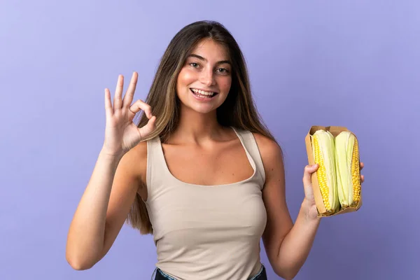 Jovem Segurando Milho Isolado Fundo Roxo Mostrando Sinal Com Dedos — Fotografia de Stock