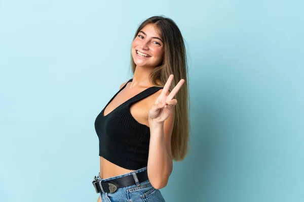 Jonge Kaukasische Vrouw Geïsoleerd Blauwe Achtergrond Glimlachen Tonen Overwinning Teken — Stockfoto