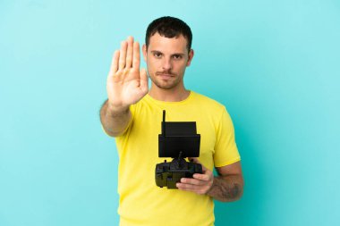 Brezilyalı adam uzaktan kumandalı uzaktan kumandayla izole edilmiş mavi arkaplanı durdurma hareketi yapıyor.