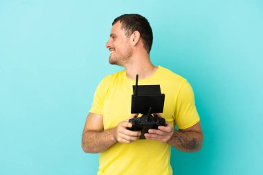 Brezilyalı bir adam uzaktan kumanda ile izole edilmiş mavi arkaplanı kontrol ediyor. Yan pozisyonda gülüyor.