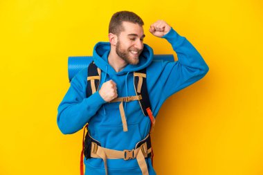 Sarı arka planda izole edilmiş büyük sırt çantalı beyaz bir dağcı zaferi kutluyor.