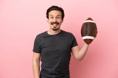 Genç beyaz adam rugby oynuyor. Pembe arka planda izole edilmiş ve yüzünde sürpriz bir ifade var.