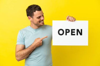 Mor arkaplan üzerinde Brezilyalı bir adam açık yazılı bir pankart tutuyor ve onu işaret ediyor.