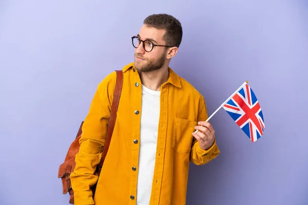 年轻的高加索男子举着一面英国国旗 呈紫色背景 向侧面望去 — 图库照片