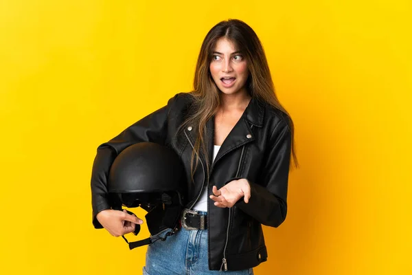 脇を見ながら驚きの表情で黄色の背景に隔離されたオートバイのヘルメットを持っている女性 — ストック写真
