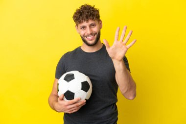 Yakışıklı genç futbolcu sarı arka planda beş parmaklı izole edilmiş.