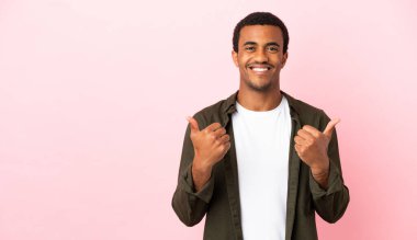 Telif uzayındaki Afro-Amerikalı adam pembe arka planda, başparmakları havada ve gülümsüyor.