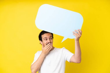 Sarı arka planda izole edilmiş genç beyaz adam elinde şaşırmış bir ifadeyle boş bir konuşma balonu tutuyor.