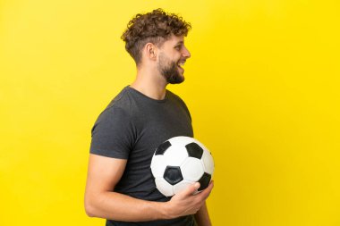 Yakışıklı genç futbolcu. Sarı arka planda izole edilmiş. Yan pozisyonda gülüyor.