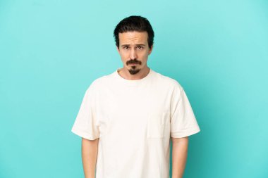 Hüzünlü bir ifadeyle mavi arka planda izole edilmiş genç beyaz bir adam.