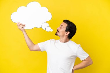 Sarı arka planda izole genç beyaz adam boş bir konuşma balonu tutuyor.