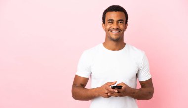 Telif uzayındaki Afrikalı Amerikalı adam pembe arka planda cep telefonuyla mesaj gönderiyor.