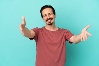 Mavi arka planda izole edilmiş genç beyaz adam sunar ve davet eder.