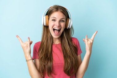 Kafkasyalı genç bir kadın mavi arka planda izole edilmiş rock hareketler yaparak müzik dinliyor.