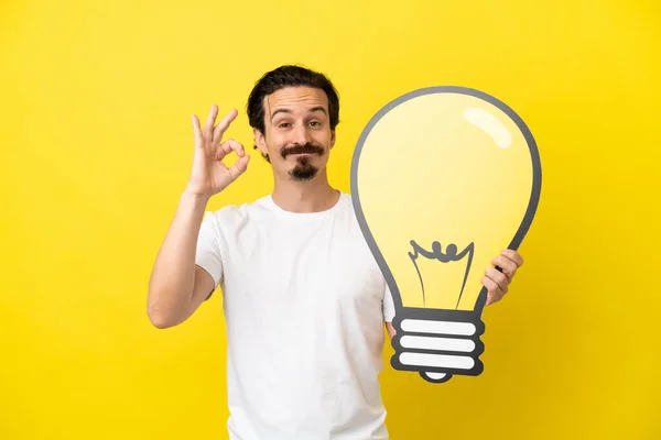 Young Caucasian Man Isolated Yellow Background Holding Bulb Icon Doing — Stock Photo, Image