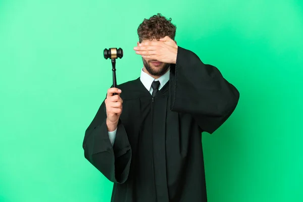 Judge over isolated green background covering eyes by hands. Do not want to see something