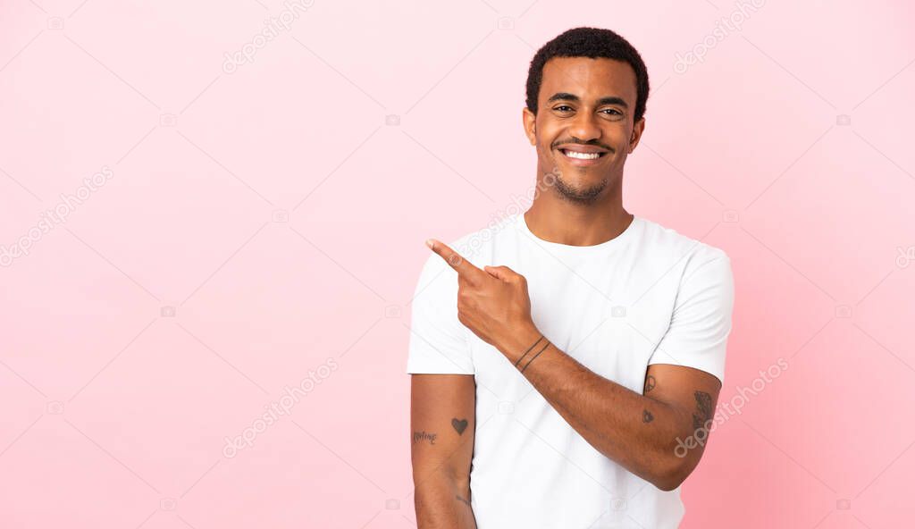 African American man on copyspace pink background pointing to the side to present a product