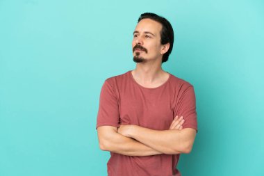 Mavi arka planda izole edilmiş genç beyaz adam yan tarafa bakıyor.