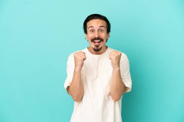 Mavi arka planda izole edilmiş genç beyaz adam galibiyeti kutluyor.