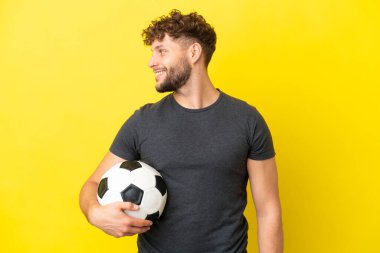 Sarı arka planda izole edilmiş yakışıklı genç futbolcu.