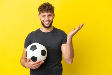 Yakışıklı genç futbolcu. Sarı arka planda izole edilmiş. Gelmesi için ellerini yana uzatıyor.