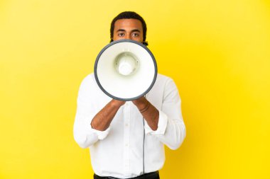 Afro-Amerikalı bir pazarlamacı, izole edilmiş sarı arka planda kulaklıkla çalışarak megafonla bağırıyor.