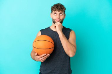 Basketbol oynayan yakışıklı genç adam mavi arka planda izole edilmiş ve yukarı bakıyor.