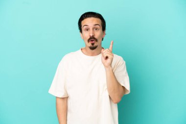 Kafkasyalı genç adam mavi arka planda izole edilmiş bir şekilde parmağını kaldırarak çözümü anlamaya çalışıyor.