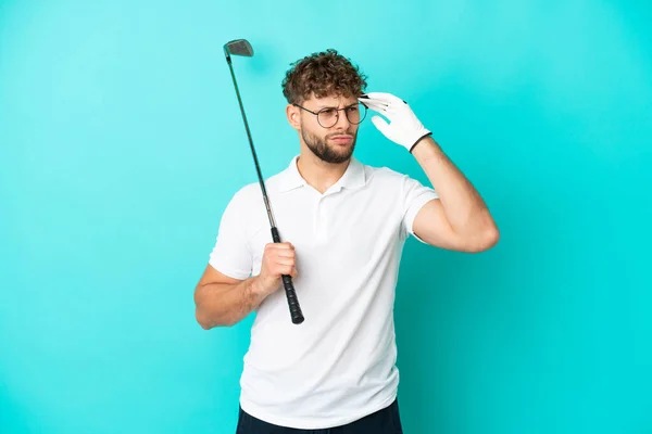 Jonge Knappe Blanke Man Geïsoleerd Blauwe Achtergrond Golfen Met Twijfels — Stockfoto