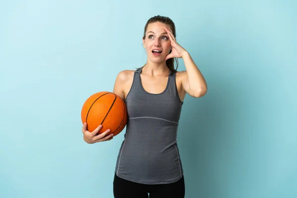 年轻女子在蓝色背景下打篮球时 一边看一边做令人惊讶的动作 — 图库照片